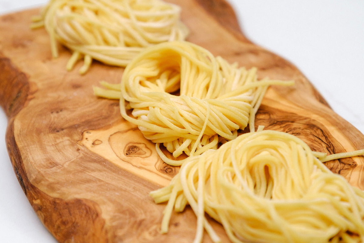 Cooked spaghetti nests arranged on a wooden cutting board.