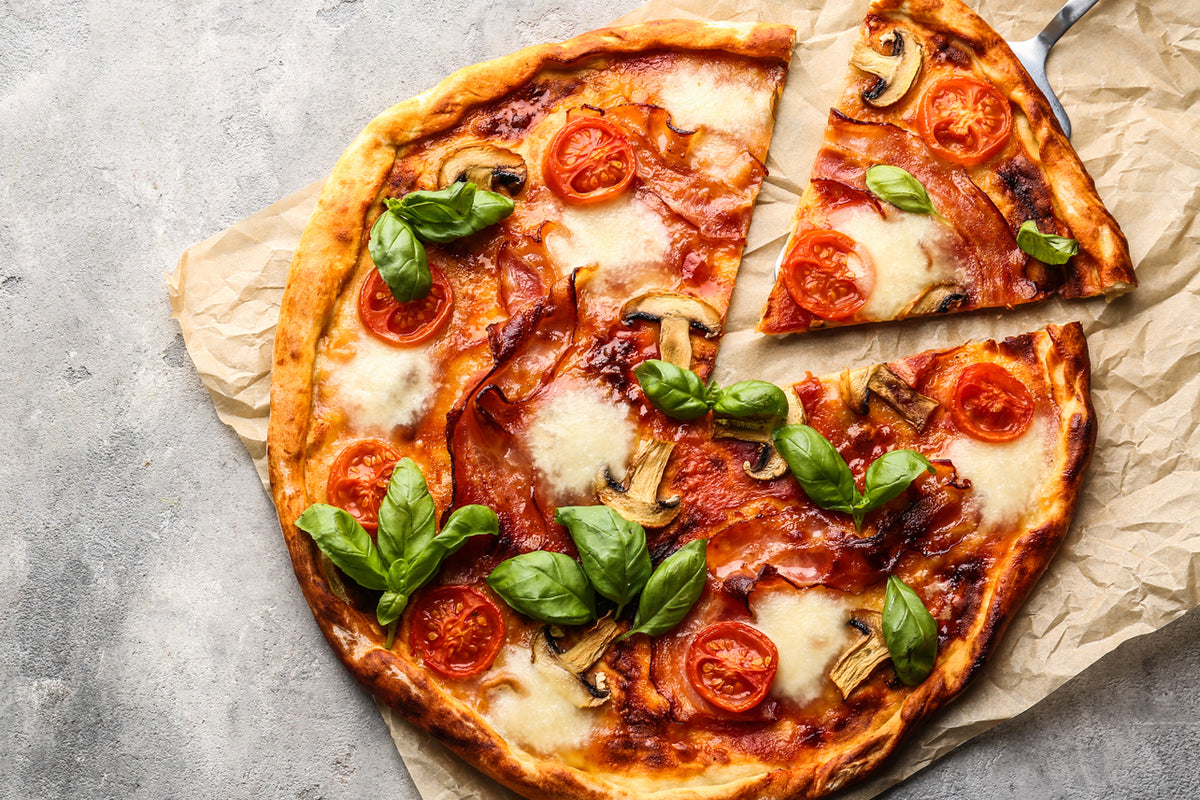 Baked pizza with tomato sauce, melted cheese, pepperoni, mushrooms, and fresh basil on parchment paper.