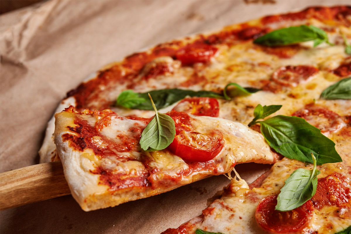 Baked pizza with melted cheese, tomato sauce, pepperoni, and fresh basil on wooden surface.