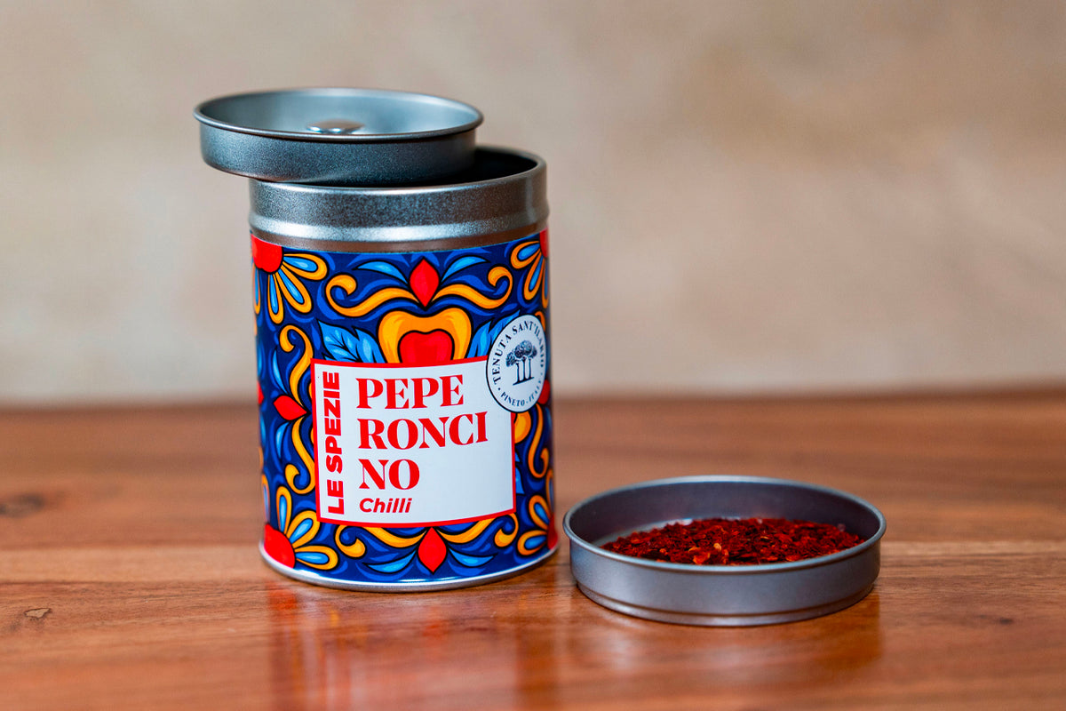 Decorative tin container with blue and red ornamental pattern labeled "Pepe Roncino Chilli" and open metal lid beside it show