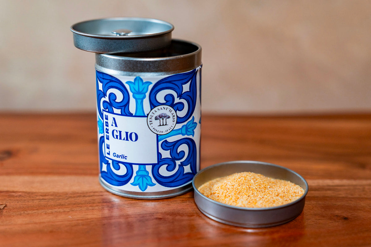 Decorative tin container with blue and white pattern labeled "Garlic" next to open dish containing granulated garlic powder.