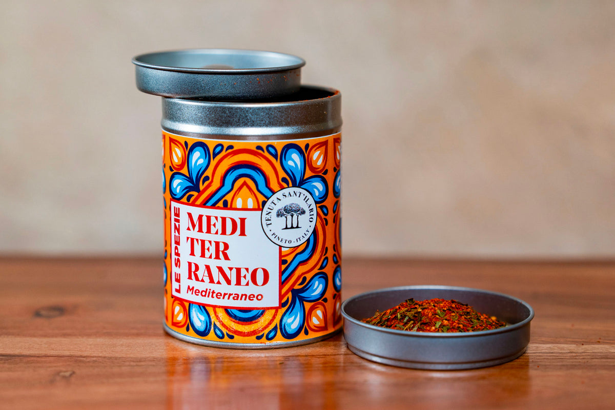 Cylindrical spice container with colorful orange and blue geometric pattern labeled "Mediterraneo" and open lid showing dried
