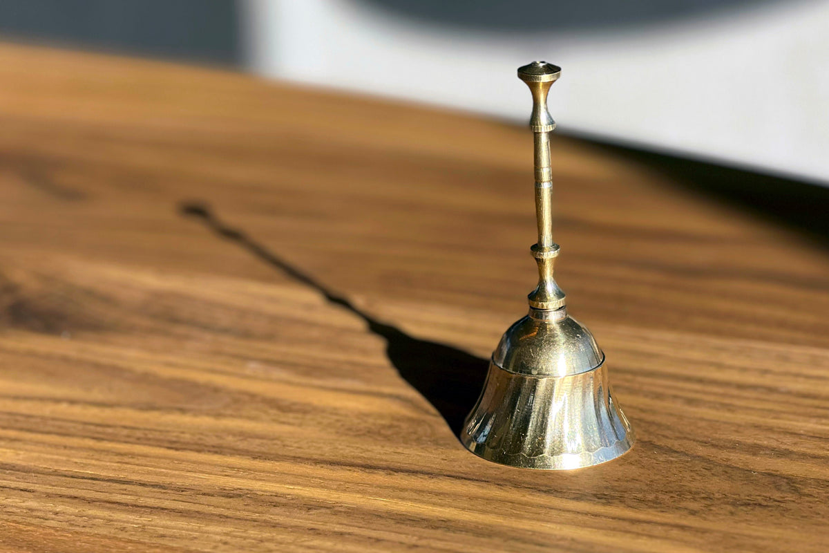 Brass bell with cylindrical handle sitting on wooden surface.