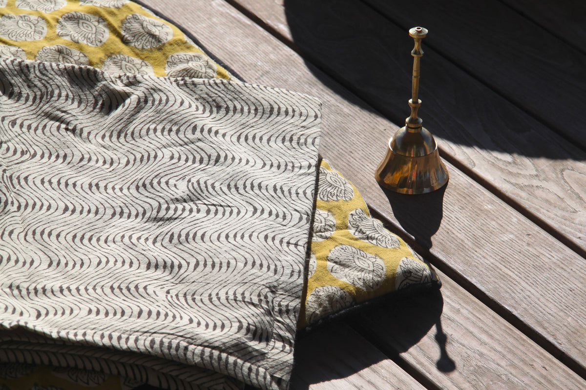 Brass meditation bell with wooden handle and striker placed on wooden deck next to patterned fabric.