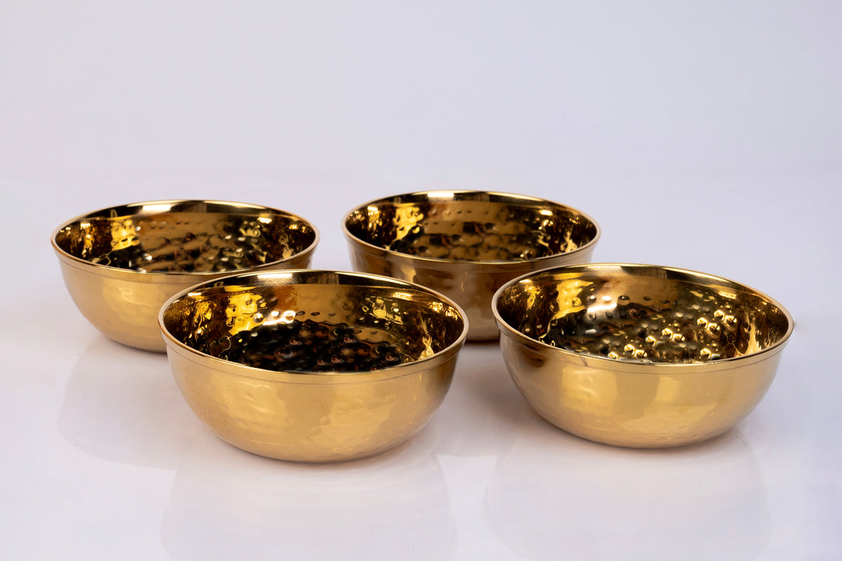 Four gold-toned stainless steel bowls with hammered texture interior surface arranged on white background.