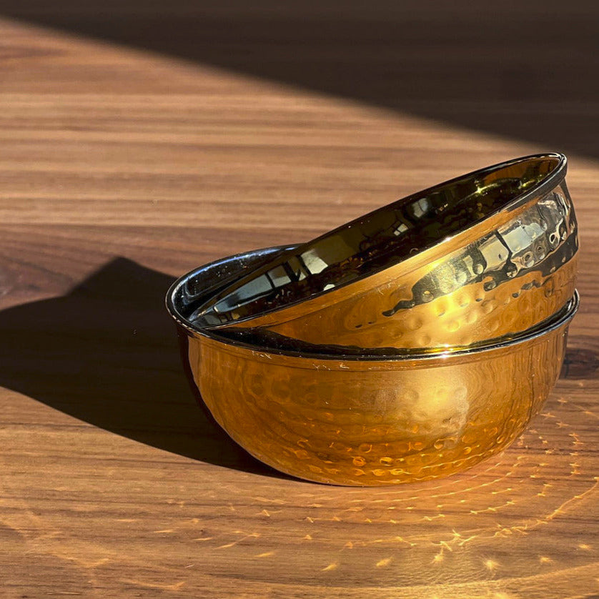 Two stainless steel bowls with hammered texture and wide rims stacked on a wooden surface.