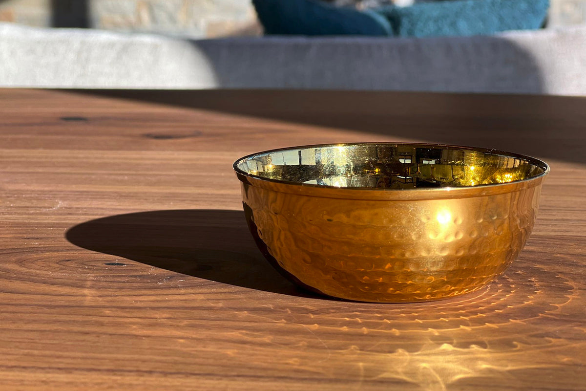 Gold-toned stainless steel bowl with hammered texture surface and polished interior rim, sitting on wooden table.