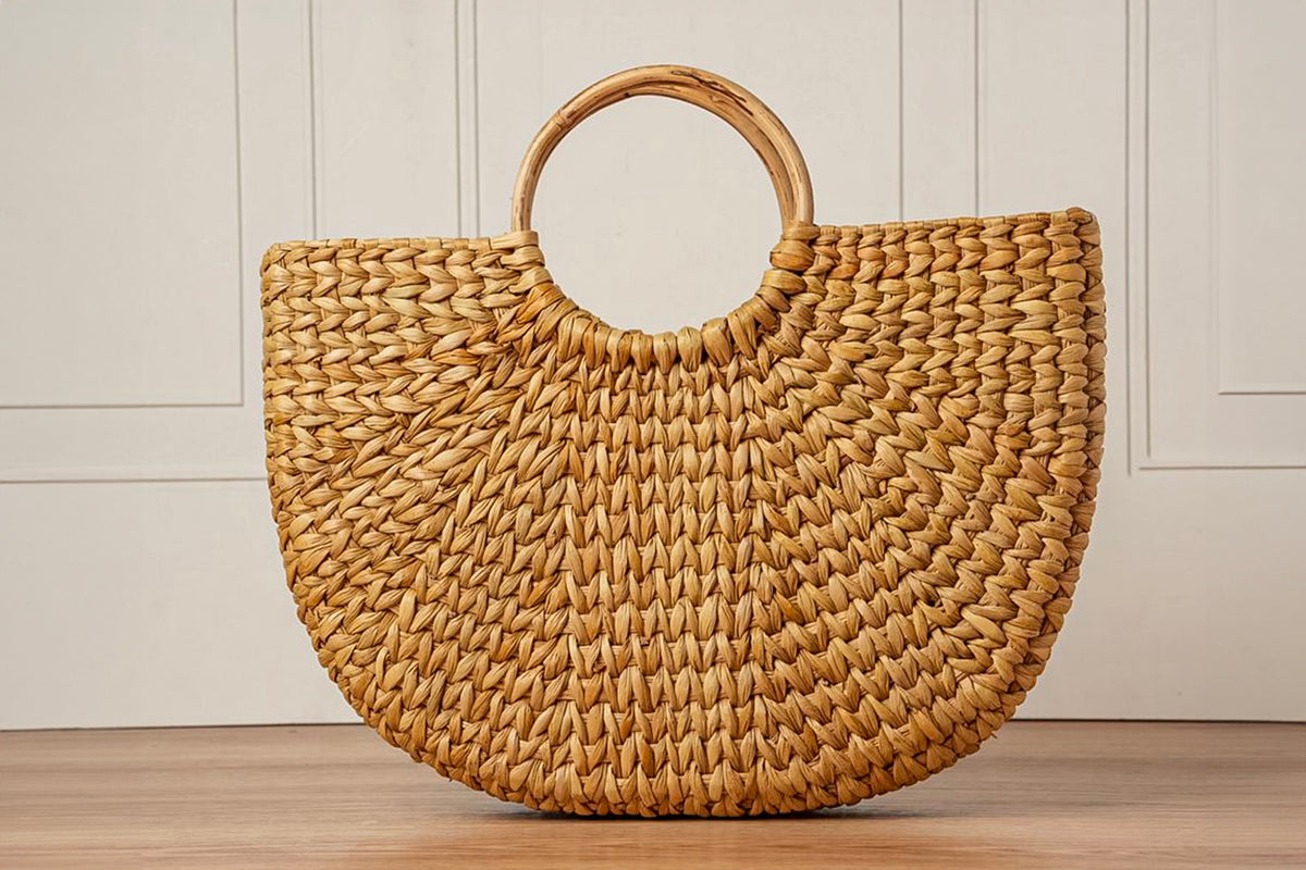 Woven straw tote bag with circular wooden handle in natural tan color.