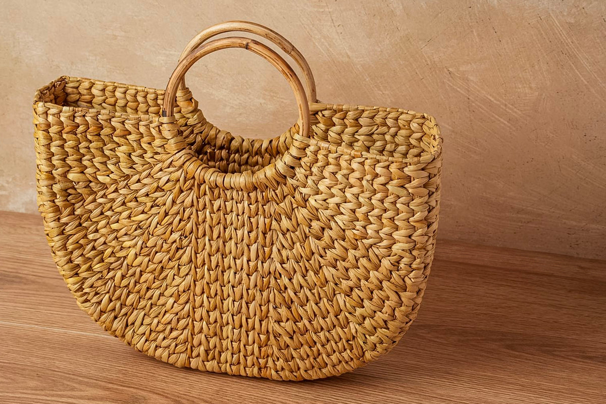 Woven straw tote bag with circular wooden handle in natural tan color.
