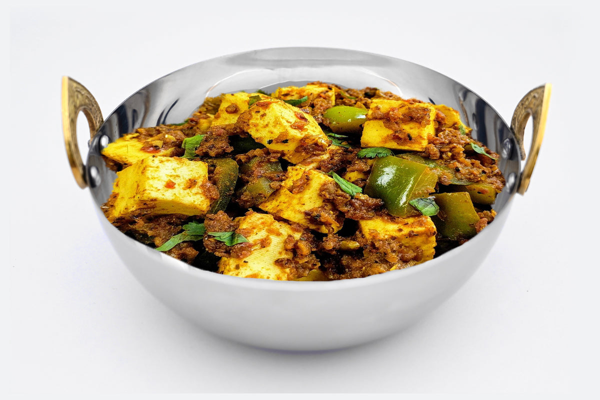 Stainless steel handi bowl with brass handles filled with spiced paneer curry dish.