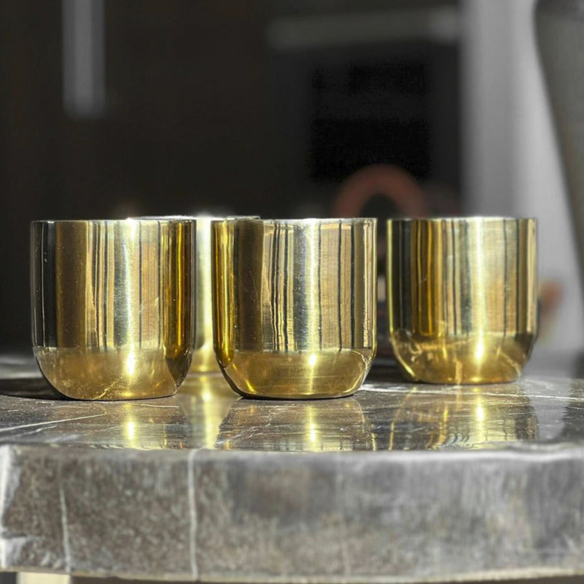 Three brass-colored double walled cups with reflective surfaces on a gray marble countertop.
