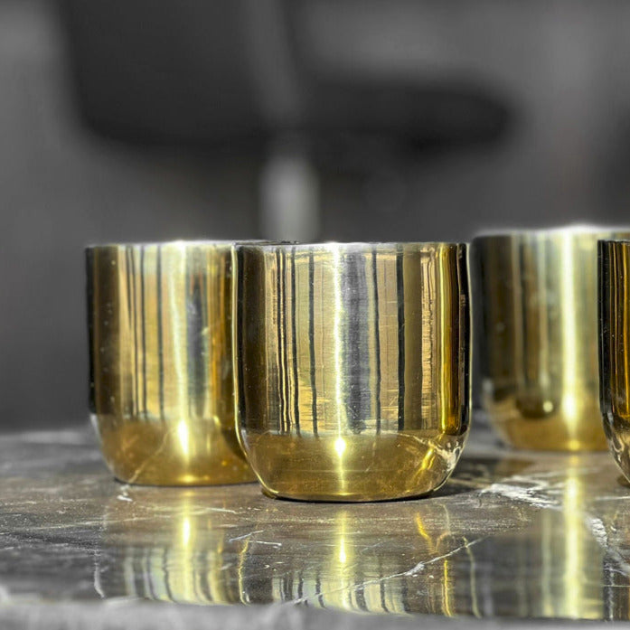 Brass-colored double walled glass cups with reflective metallic finish, displayed on a gray surface.