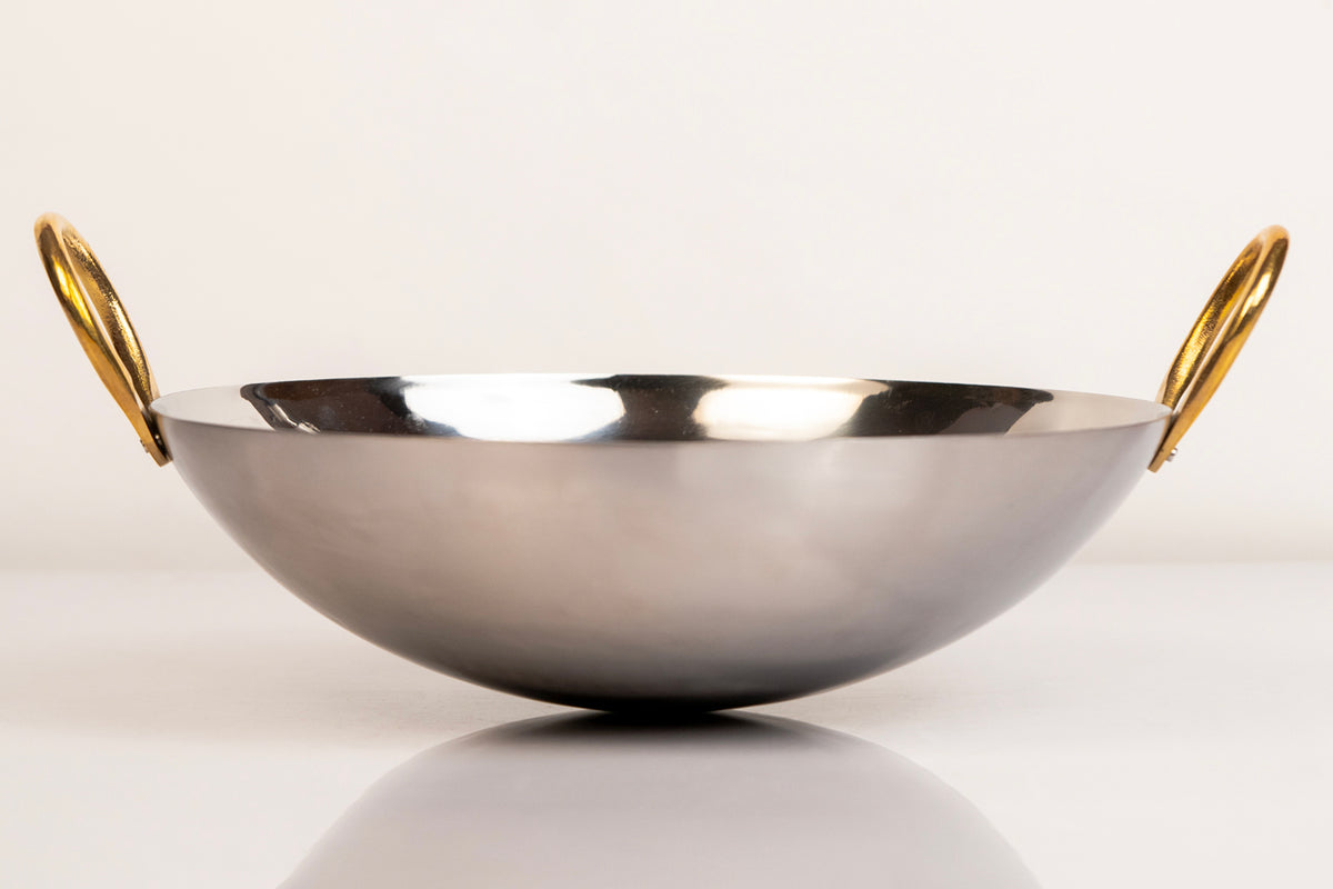 Stainless steel wok with curved bowl shape and gold brass handles on each side.