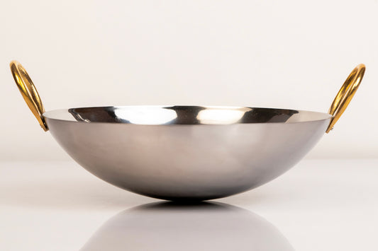 Stainless steel wok with curved bowl shape and gold brass handles on each side.