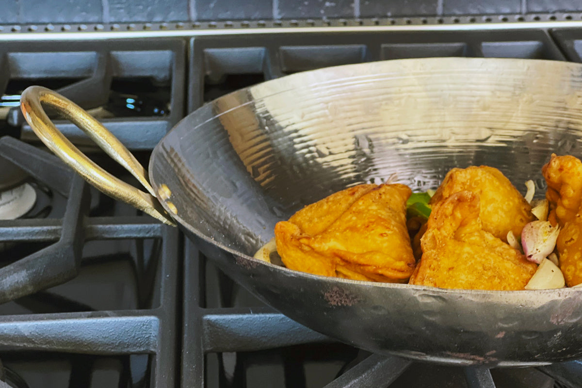 Stainless steel wok with brass handles containing fried food on stovetop.