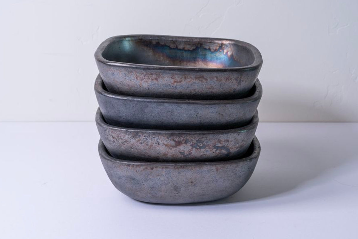 Stack of four dark gray square pottery bowls with rounded corners and rustic surface texture.