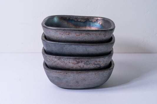 Stack of four dark gray square pottery bowls with rounded corners and rustic surface texture.