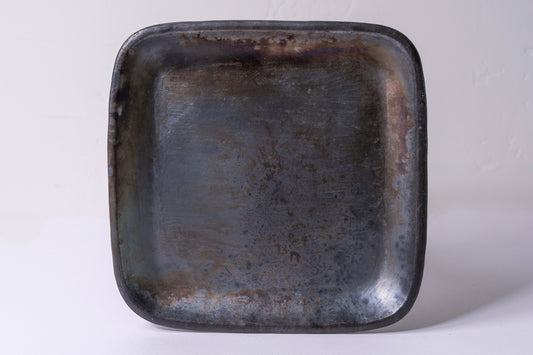 Dark gray-black handmade ceramic plate with rounded square shape and unglazed textured surface.