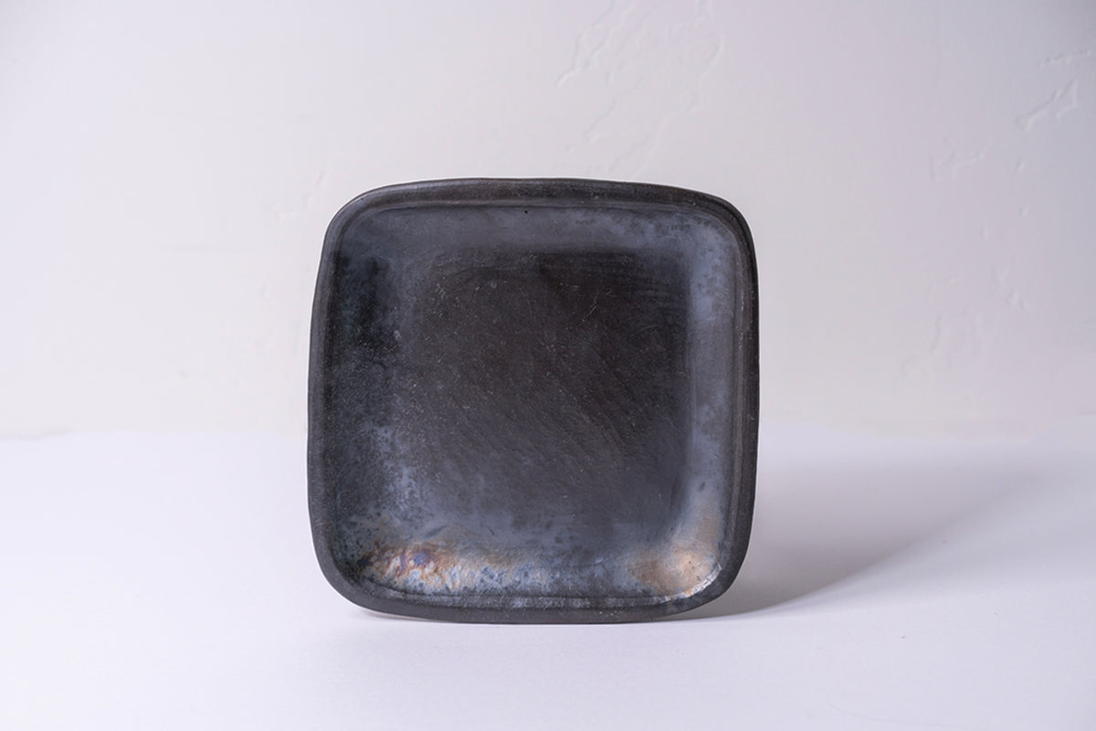 Dark gray handmade pottery plate with rounded square shape and textured surface.
