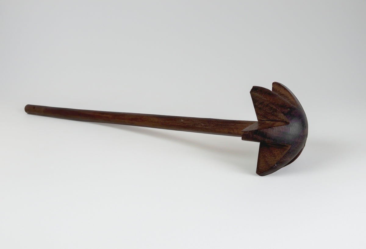 Wooden whisk with dark brown handle and paddle-shaped head with vertical slats for stirring.