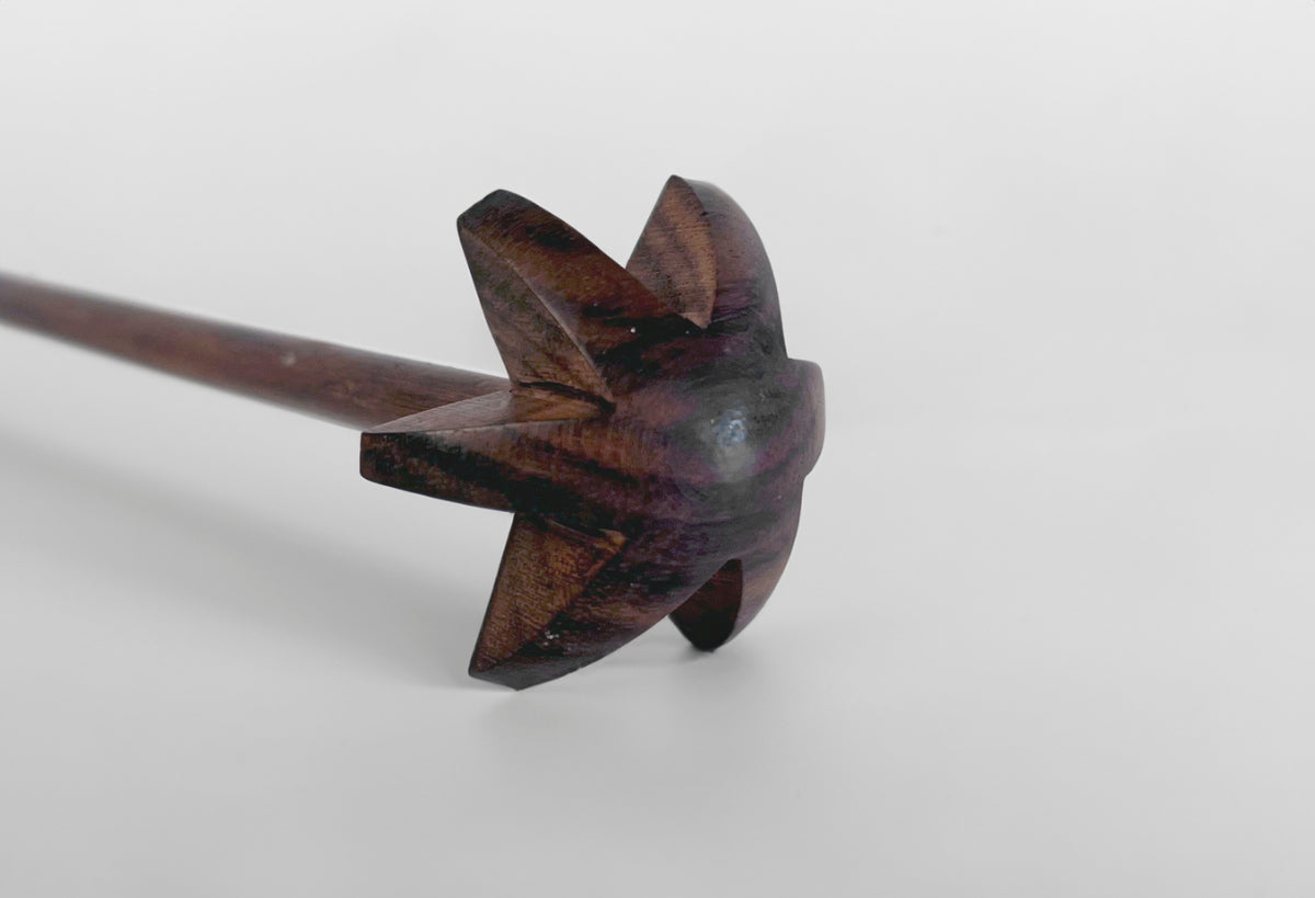 Dark wooden whisk with four flat paddles attached to a long wooden handle.