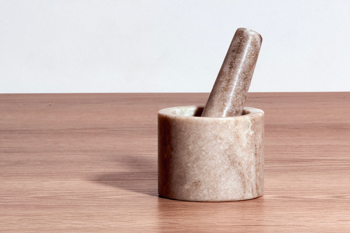 Cylindrical marble mortar with matching pestle resting inside on wooden surface.