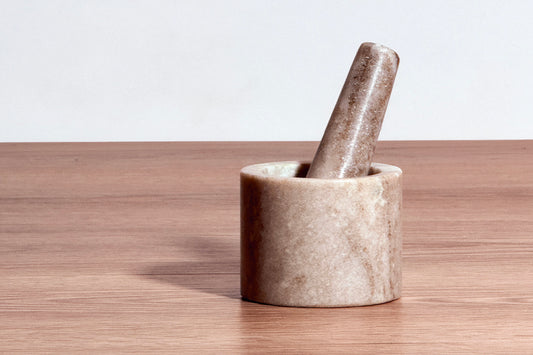 Cylindrical marble mortar with matching pestle resting inside on wooden surface.
