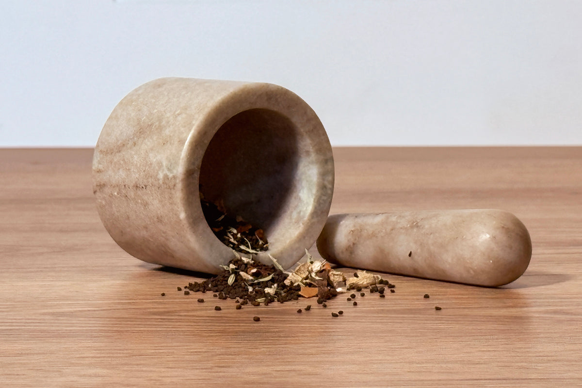 Beige marble mortar and pestle with crushed spices spilling out, displayed on wooden surface.