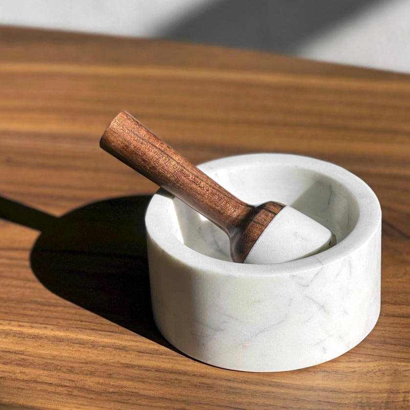 White marble mortar with wooden pestle featuring a cylindrical handle, placed on a wood surface.