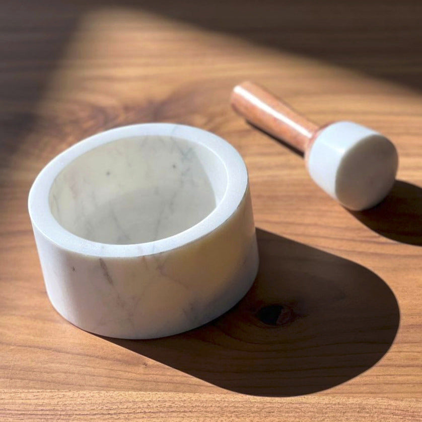 White marble mortar with matching pestle featuring a copper-colored handle, displayed on a wooden surface.