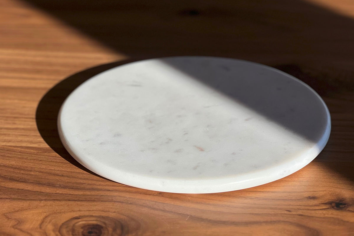 White marble round board with veined surface on wooden table.