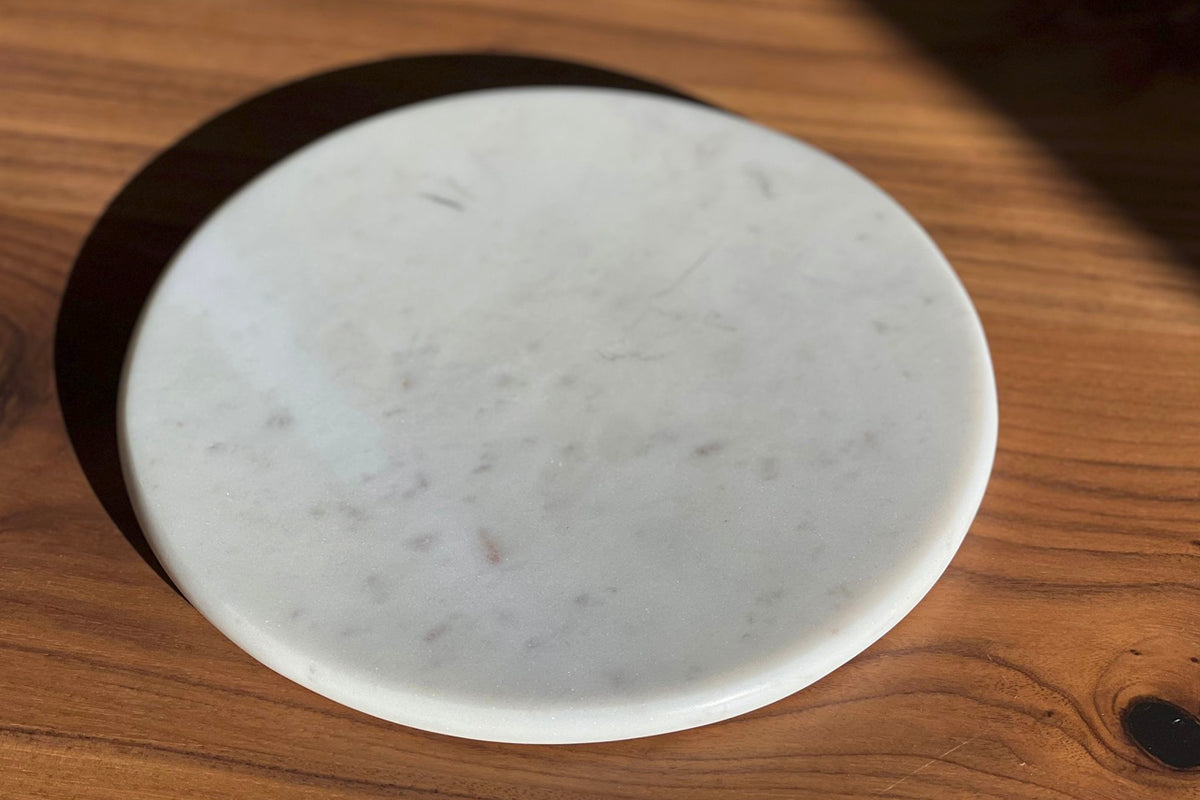 White marble circular board with gray veining on wooden surface.
