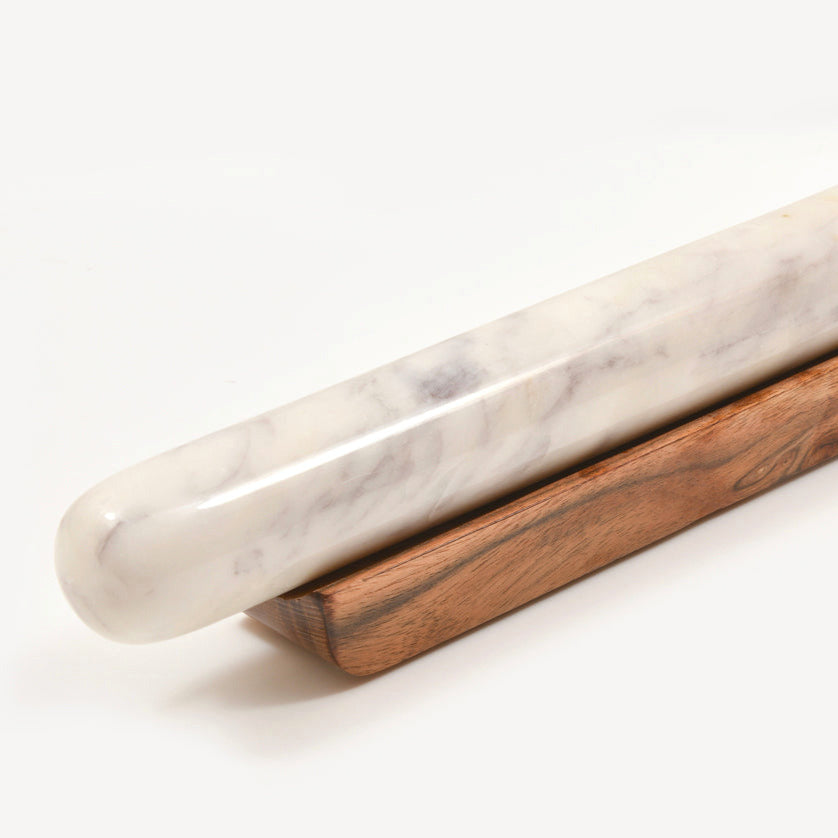 White marble rolling pin with gray veining resting in a dark wood base.