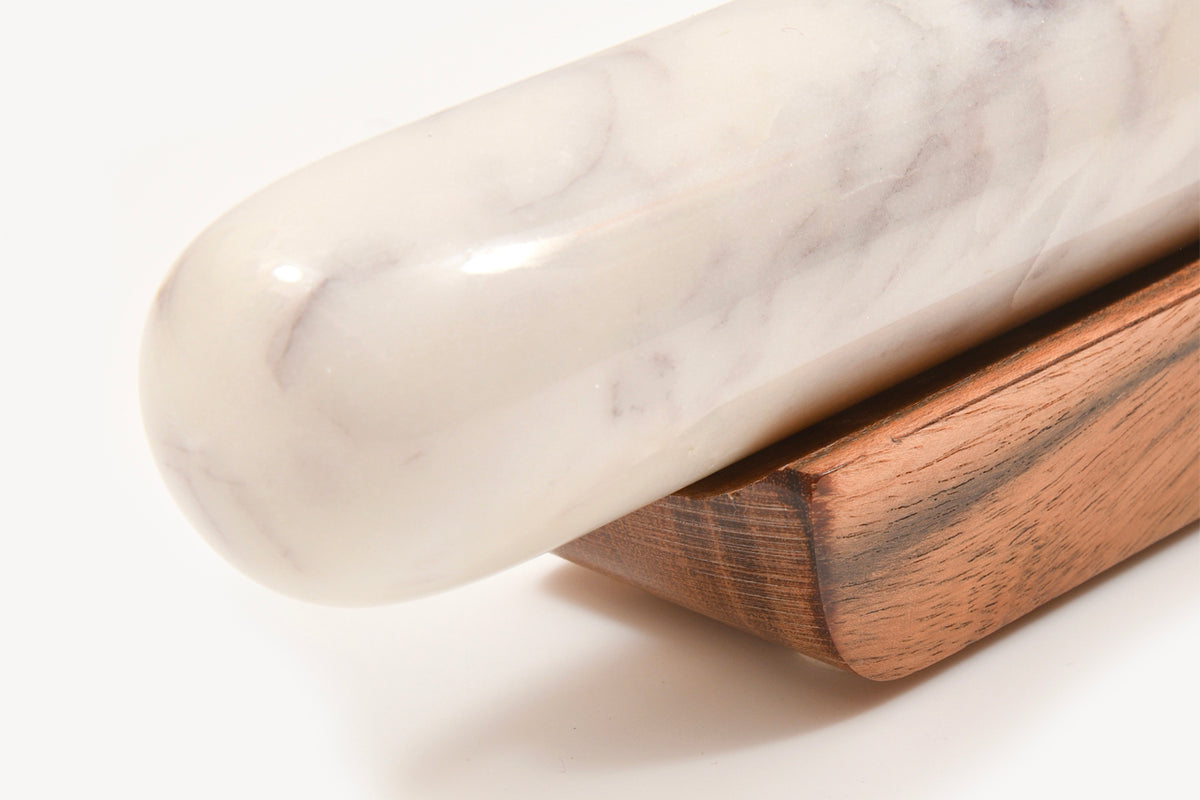 White marble rolling pin with gray veining resting on a brown wood base.