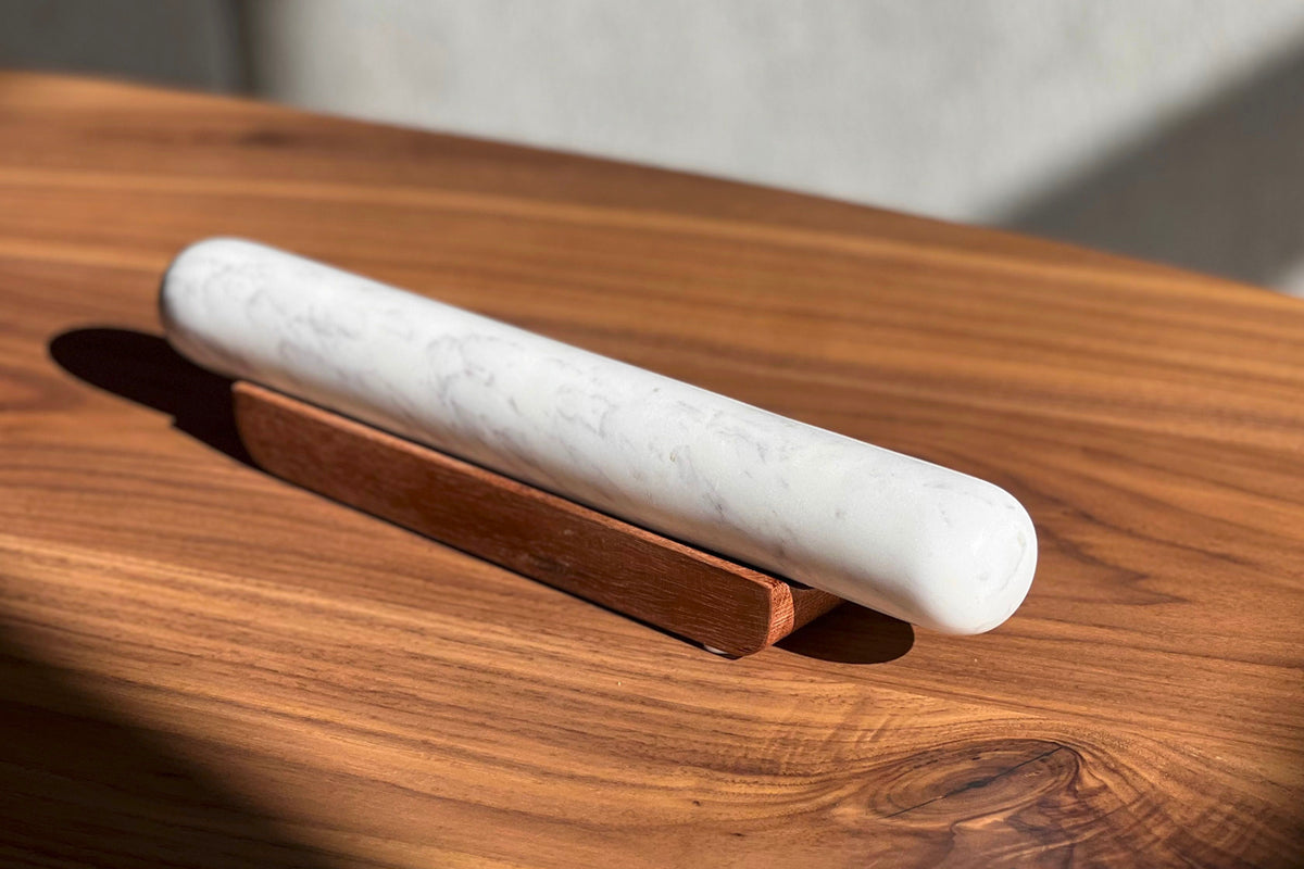 White marble rolling pin resting in a wooden base on a wood surface.