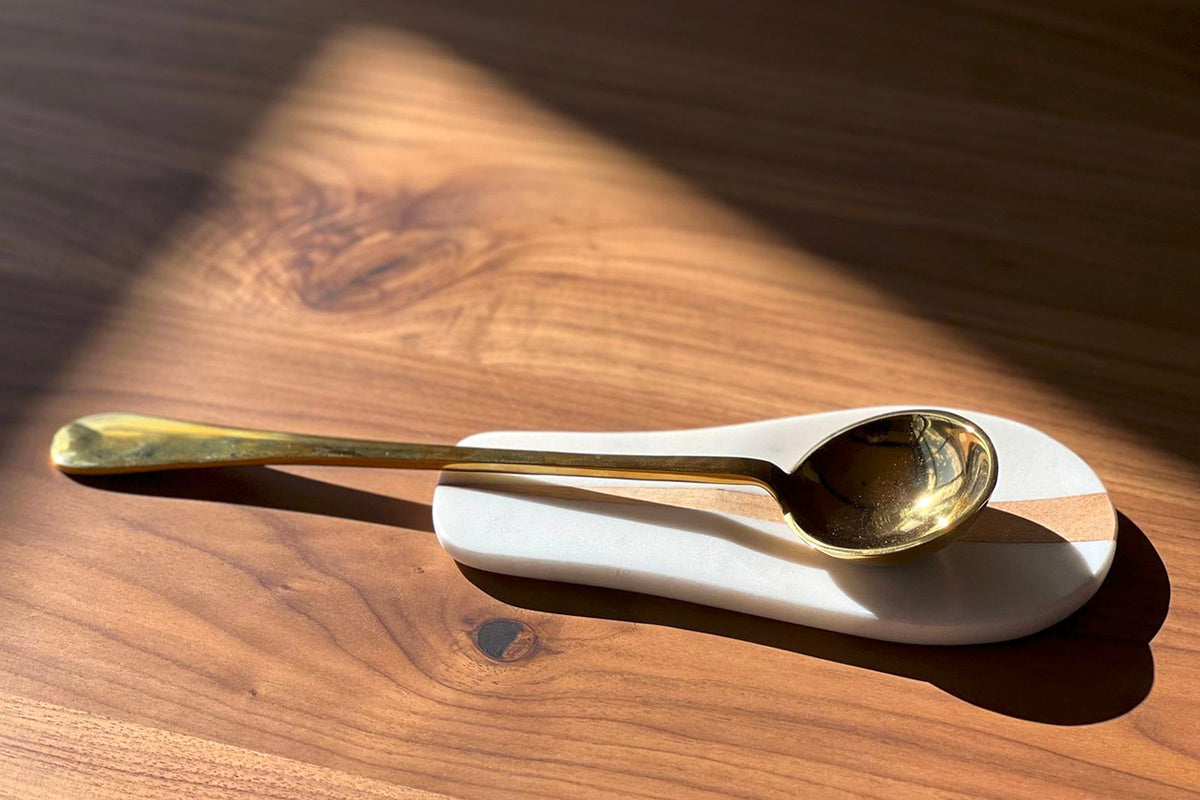 White marble spoon rest with brass spoon on wooden surface.