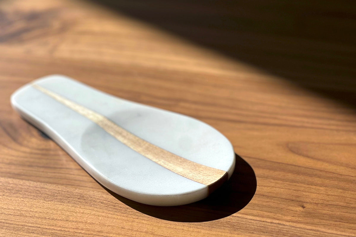 White marble spoon rest with natural wood accent stripe, oval shape on wooden surface.