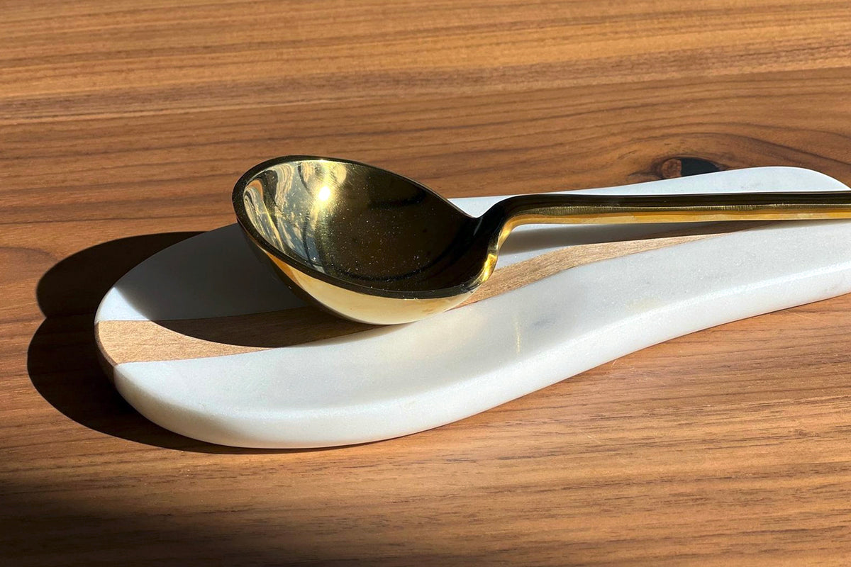 White marble spoon rest with gold-trimmed spoon featuring black bowl on wooden surface.