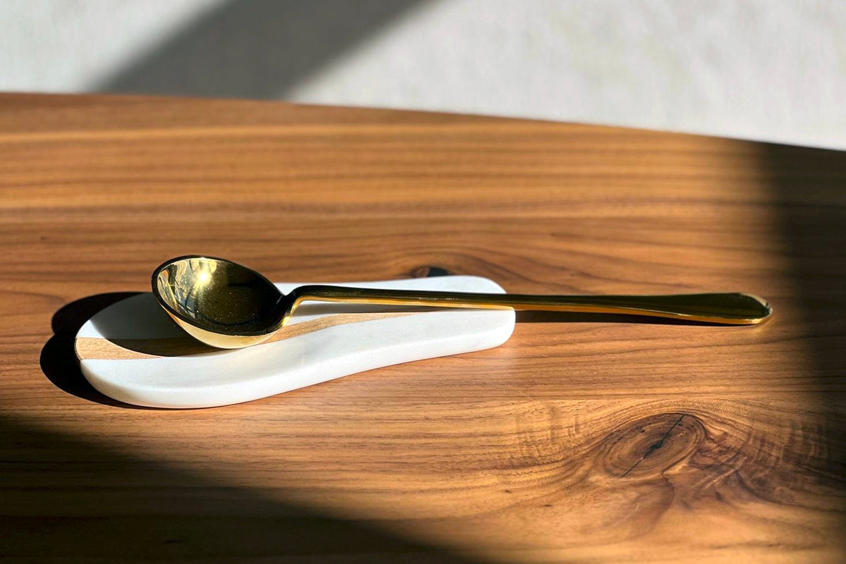 Gold-plated spoon resting on white marble rest against wooden surface.