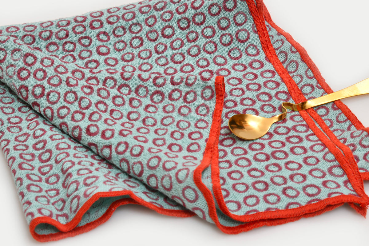 Gray napkins with red circle block print pattern and red binding edges, displayed with gold spoon.