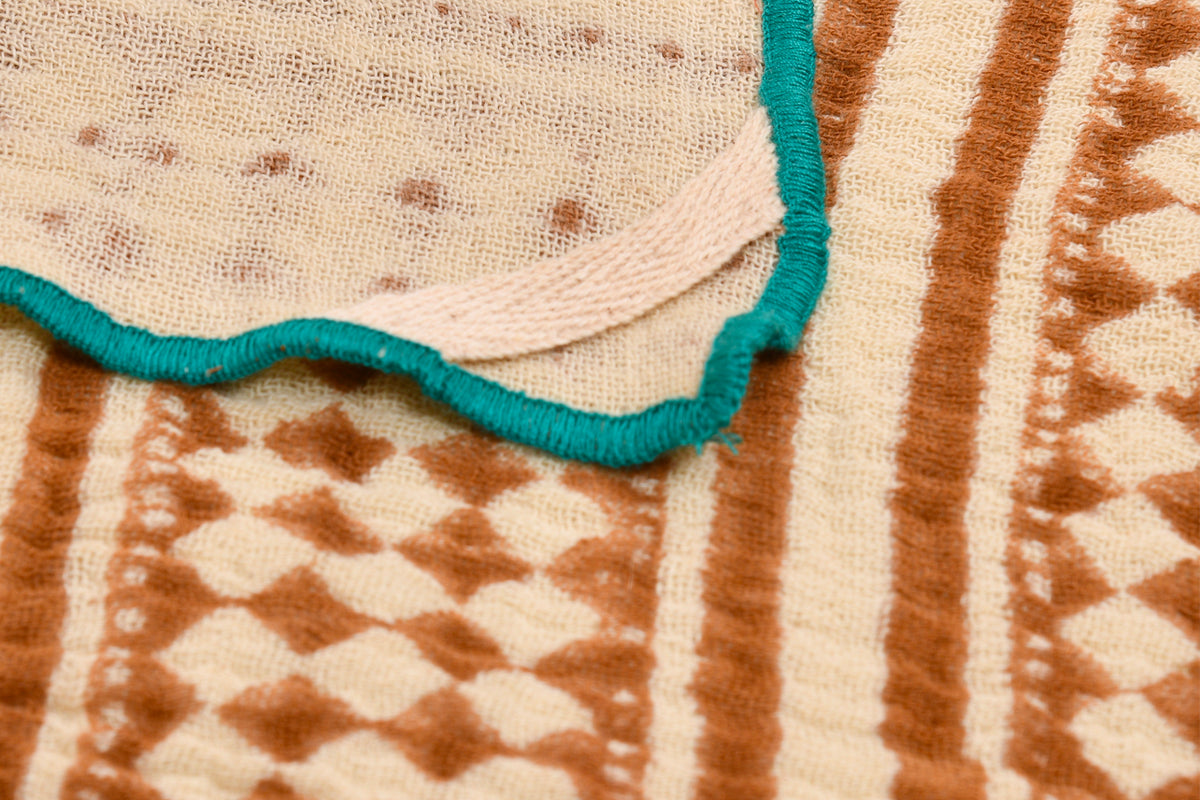 Cream and rust block print napkins with teal bound edges and geometric woven patterns.
