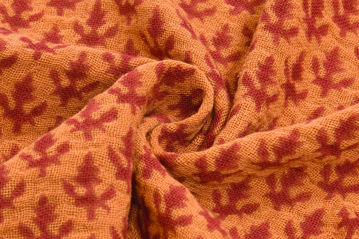 Woven fabric with red and gold block print pattern showing textured surface and folds.