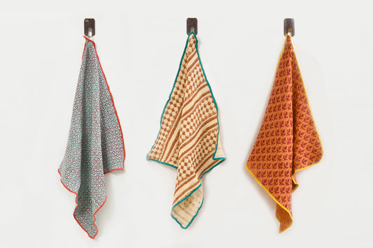 Three napkins with block-printed geometric patterns in blue, tan, and orange with contrasting colored borders.