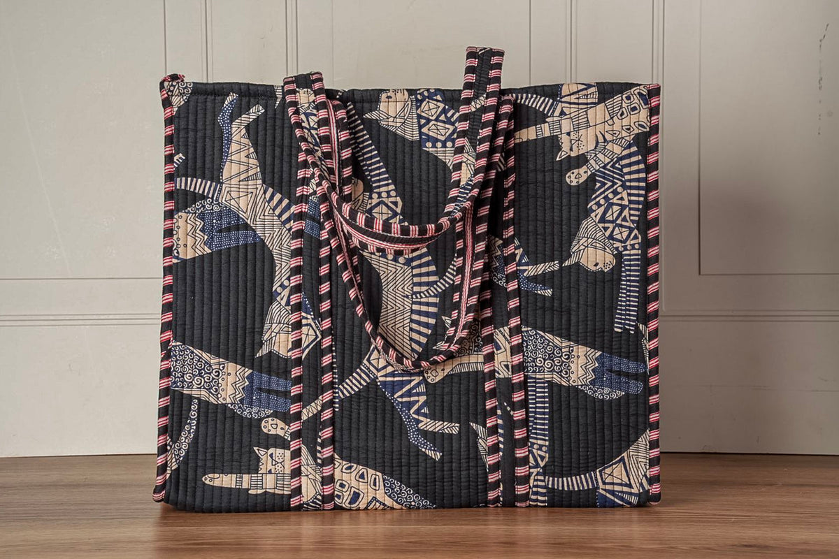 Quilted tote bag with cat-face pattern in black, cream, and pink with striped handles.