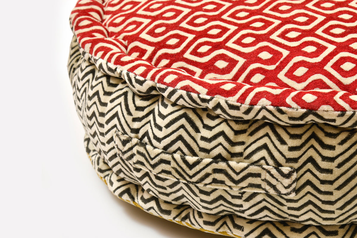 Round meditation cushion with red geometric block print on top and black zigzag pattern on cream side.