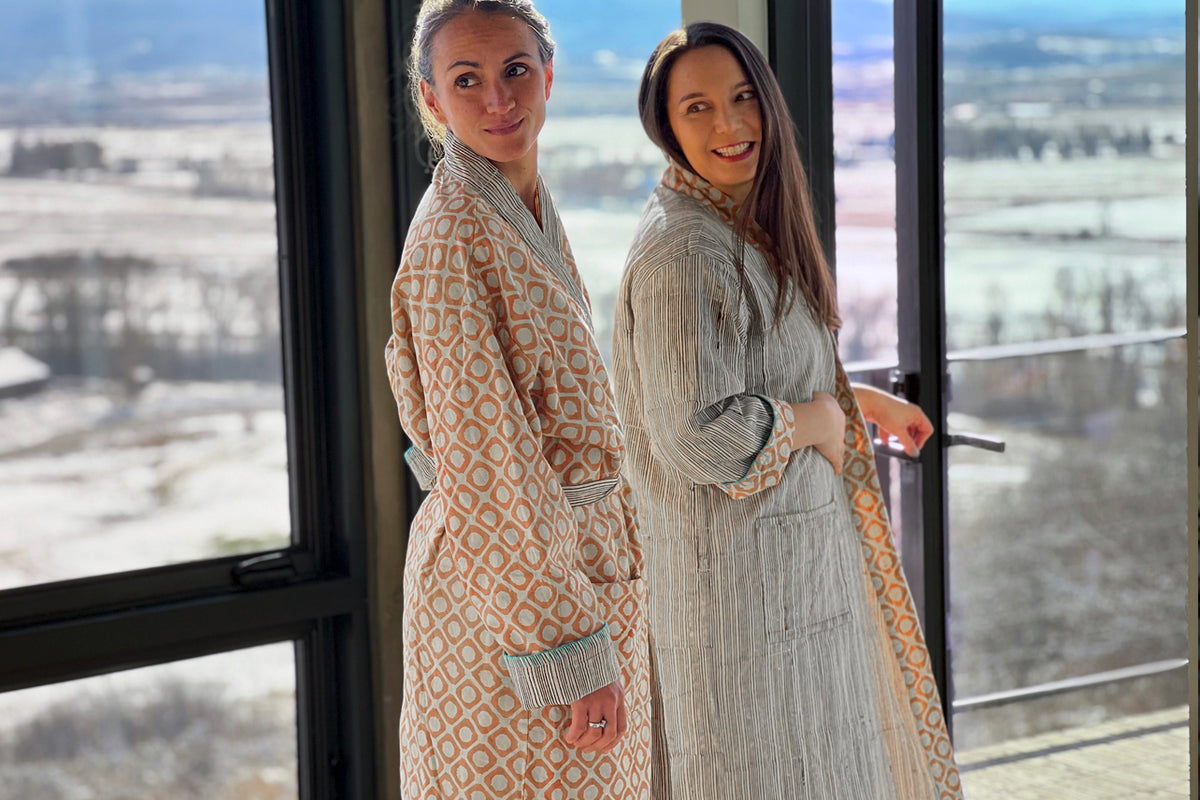 Two women wearing reversible robes with block print geometric patterns on one side and striped design on the reverse.