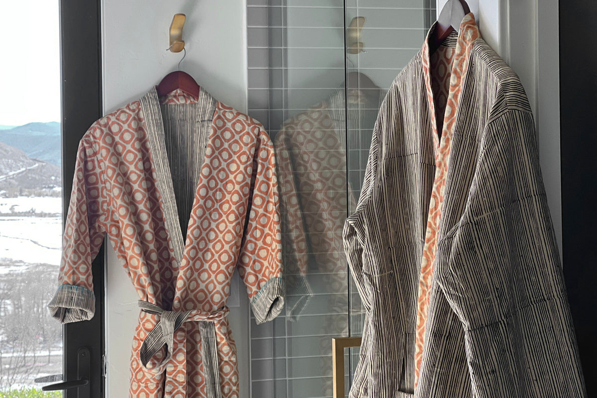 Two reversible robes displayed on hangers, showing block print patterns in rust and cream tones on one side and striped desig