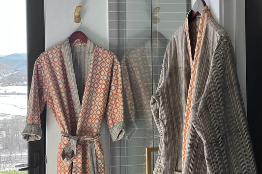 Two reversible robes displayed on hangers, showing block print patterns in rust and cream tones on one side and striped desig