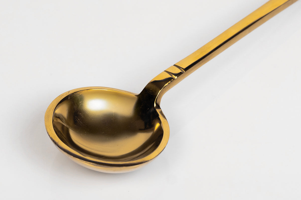 Gold-toned serving spoon with rounded bowl-shaped head and long handle with decorative black bands.