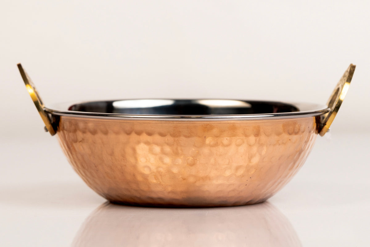 Hammered copper serving bowl with brass handles and dark interior lining.